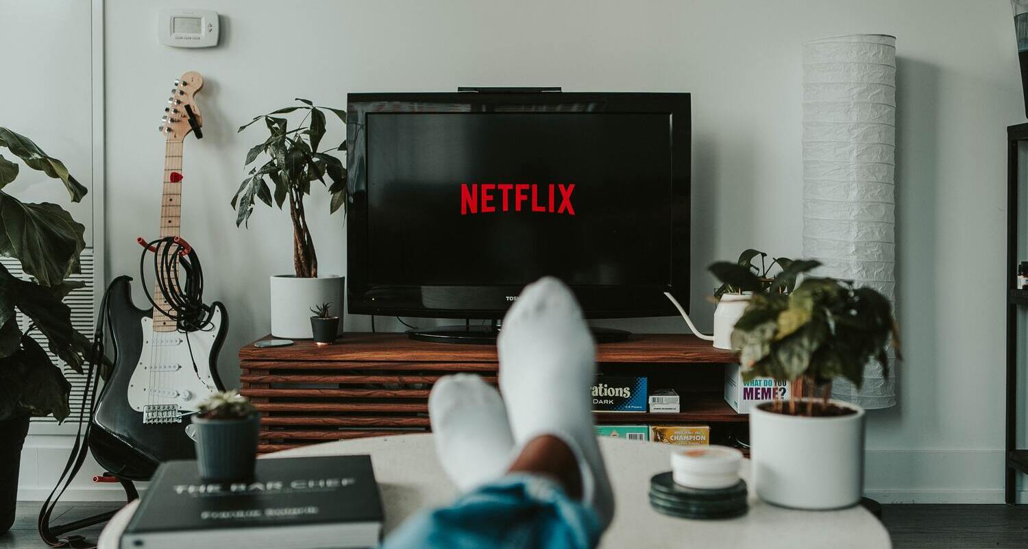 Person sitzt mit auf dem Tisch ausgestreckten Füßen im Wohnzimmer und schaut Netflix.