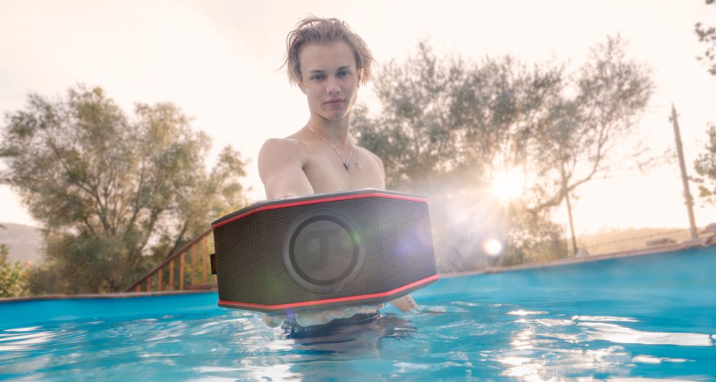 Młody mężczyzna na basenie z głośnikiem Bluetooth Rockster Go 2 w ręce