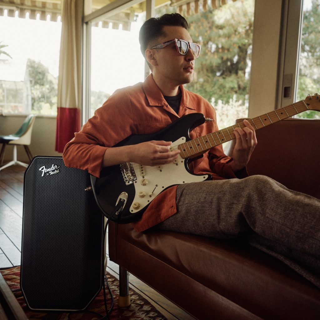 Mann sitzt auf dem Sofa und spielt E-Gitarre, die an einen Fender x Teufel ROCKSTER AIR 2 angeschlossen ist